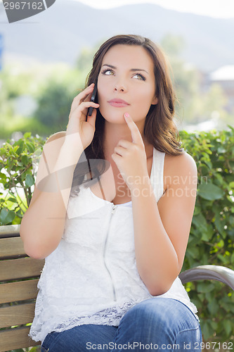 Image of Young Adult Female Talking on Cell Phone Outdoors on Bench