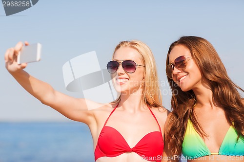 Image of two smiling women making selfie on beach