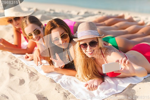 Image of group of smiling women with smartphone on beach