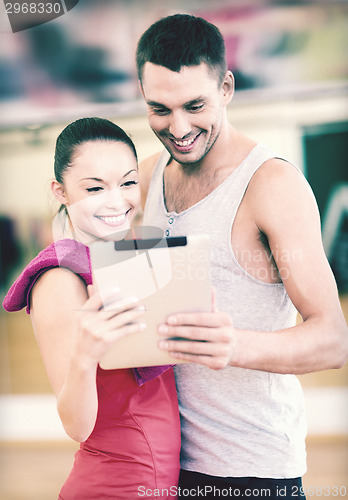 Image of two smiling people with tablet pc in the gym