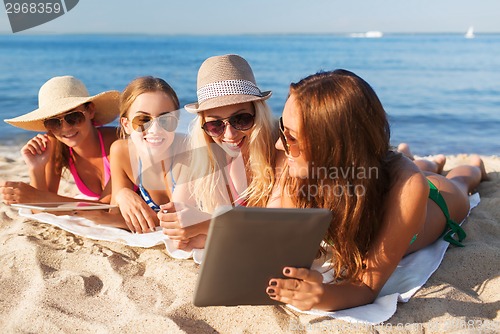 Image of group of smiling young women with tablets on beach