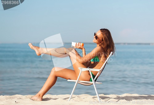 Image of smiling young woman sunbathing in lounge on beach