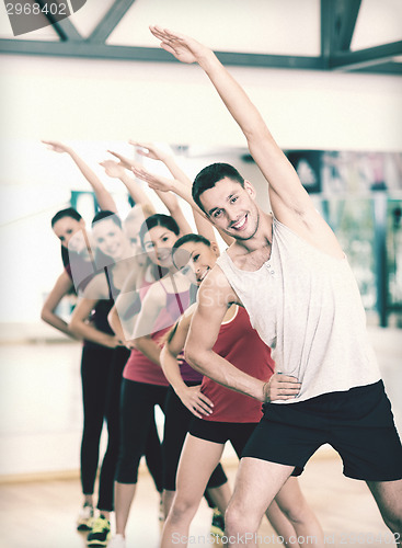 Image of group of smiling people stretching in the gym