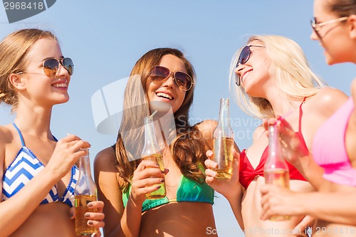 Image of group of smiling young women drinking on beach