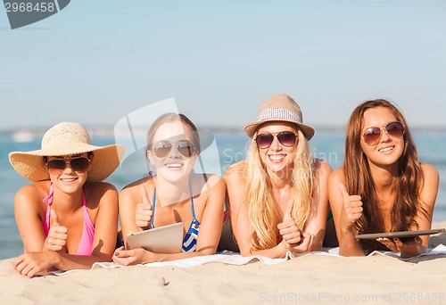 Image of group of smiling young women with tablets on beach