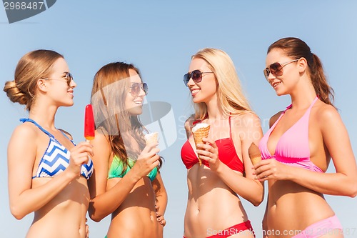 Image of group of smiling women eating ice cream on beach