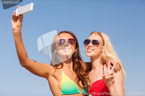 Image of two smiling women making selfie on beach