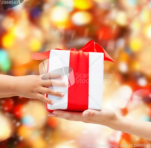 Image of close up of child and mother hands with gift box
