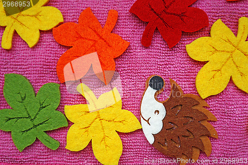 Image of Hedgehog and colorful Maple leaves out of felt on a pink fabric 