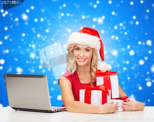 Image of smiling woman in santa hat with gifts and laptop