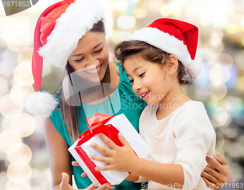 Image of happy mother and girl in santa hats with gift box