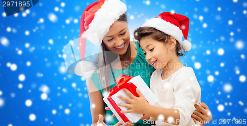 Image of happy mother and girl in santa hats with gift box