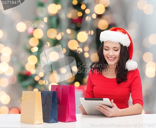 Image of smiling woman in santa hat with bags and tablet pc
