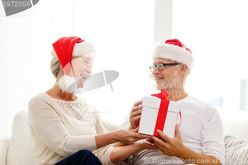 Image of happy senior couple in santa hats with gift box