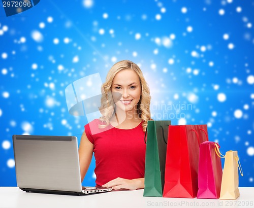 Image of smiling woman in red dress with gifts and laptop