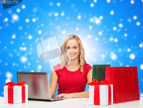 Image of smiling woman in red shirt with gifts and laptop