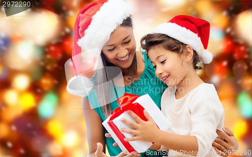 Image of happy mother and girl in santa hats with gift box