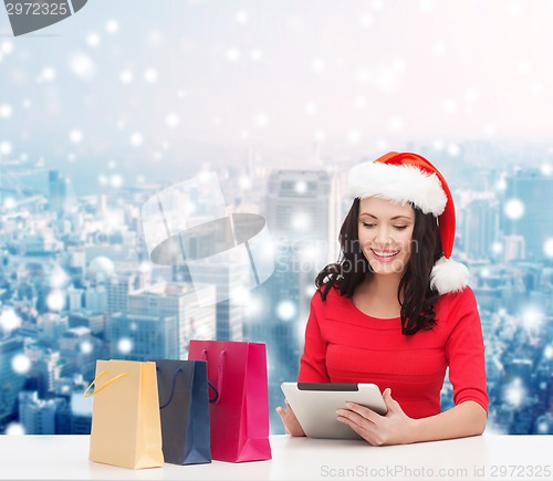 Image of smiling woman in santa hat with bags and tablet pc