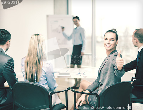Image of businesswoman with team showing thumbs up