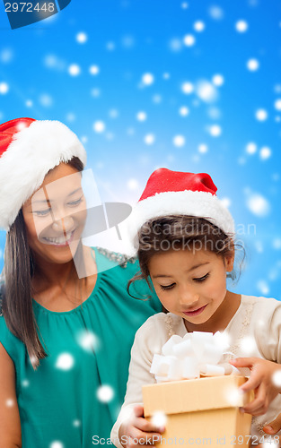 Image of happy mother and girl in santa hats with gift box