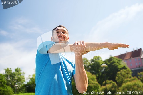Image of smiling man stretching outdoors
