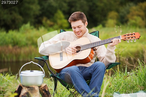 Image of smiling man with guitar and dixie in camping