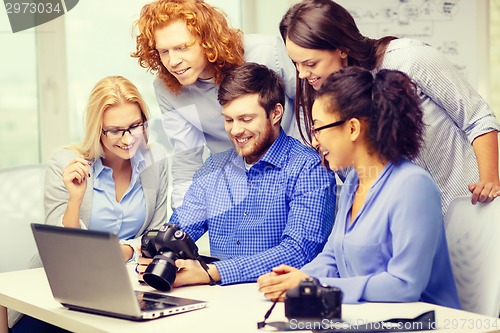 Image of smiling team with laptop and photocamera in office