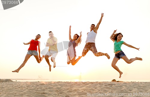 Image of smiling friends dancing and jumping on beach