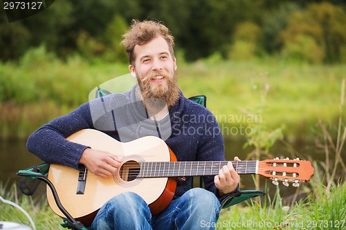 Image of smiling man playing guitar in camping