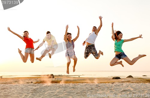 Image of smiling friends dancing and jumping on beach