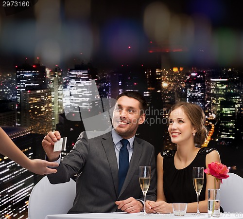 Image of smiling couple paying for dinner with credit card