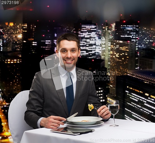 Image of smiling man with tablet pc eating main course