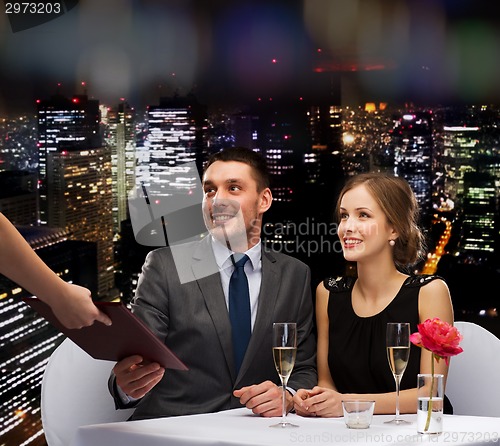 Image of waiter giving menu to happy couple at restaurant