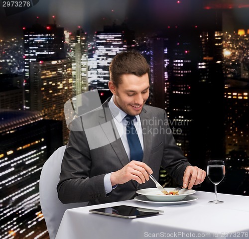 Image of smiling man with tablet pc eating main course