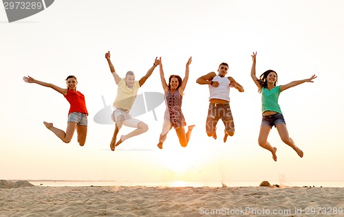 Image of smiling friends dancing and jumping on beach