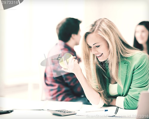 Image of smiling student girl eating apple at school