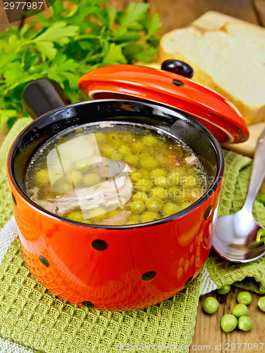 Image of Soup from green peas with meat in red bowl and bread on board