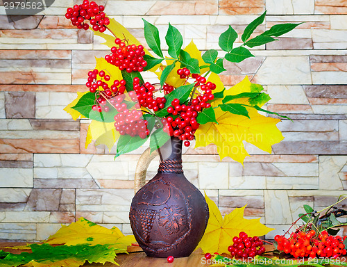 Image of Autumn still life: berries and autumn leaves in a ceramic vase.