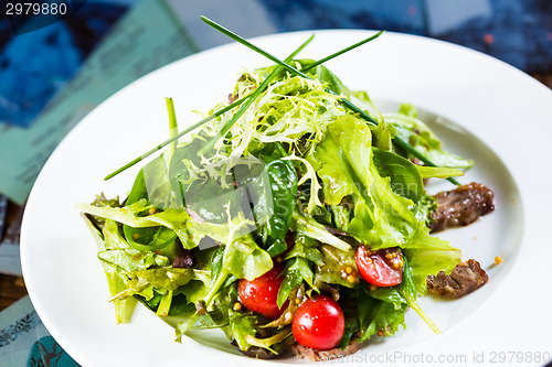 Image of Fresh vegetable salad with meat and cherry tomatoes on white plate.