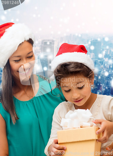 Image of happy mother and girl in santa hats with gift box