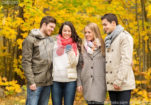 Image of smiling friends with smartphones in city park