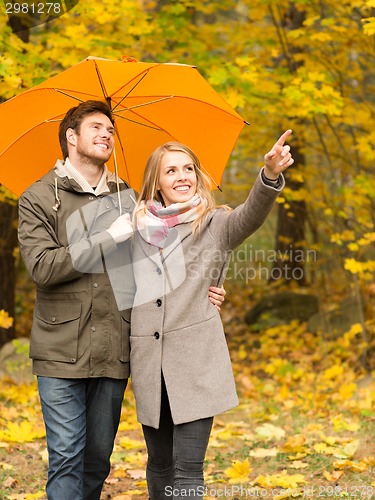 Image of smiling couple with umbrella in autumn park