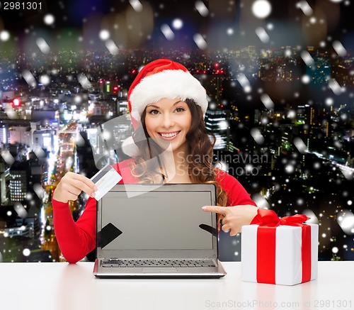 Image of smiling woman in santa hat with gift and laptop