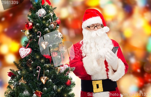 Image of santa claus with smartphone and christmas tree