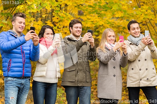 Image of smiling friends with smartphones in city park