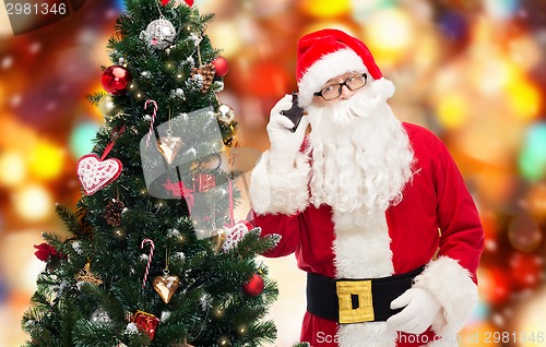Image of santa claus with smartphone and christmas tree
