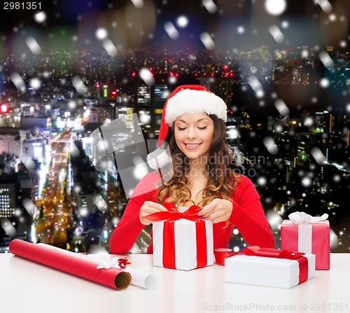 Image of smiling woman in santa helper hat packing gifts