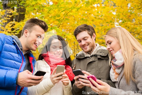 Image of smiling friends with smartphones in city park