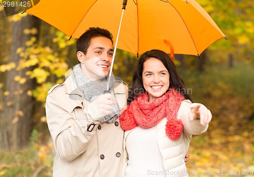 Image of smiling couple with umbrella in autumn park