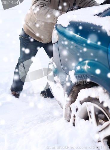 Image of closeup of man pushing car stuck in snow